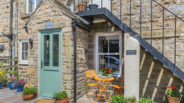 Une charmante maison en pierre avec une porte verte, un petit espace extérieur aménagé avec une table et des chaises, et un panneau indiquant l’emplacement réservé au stationnement des clients.
