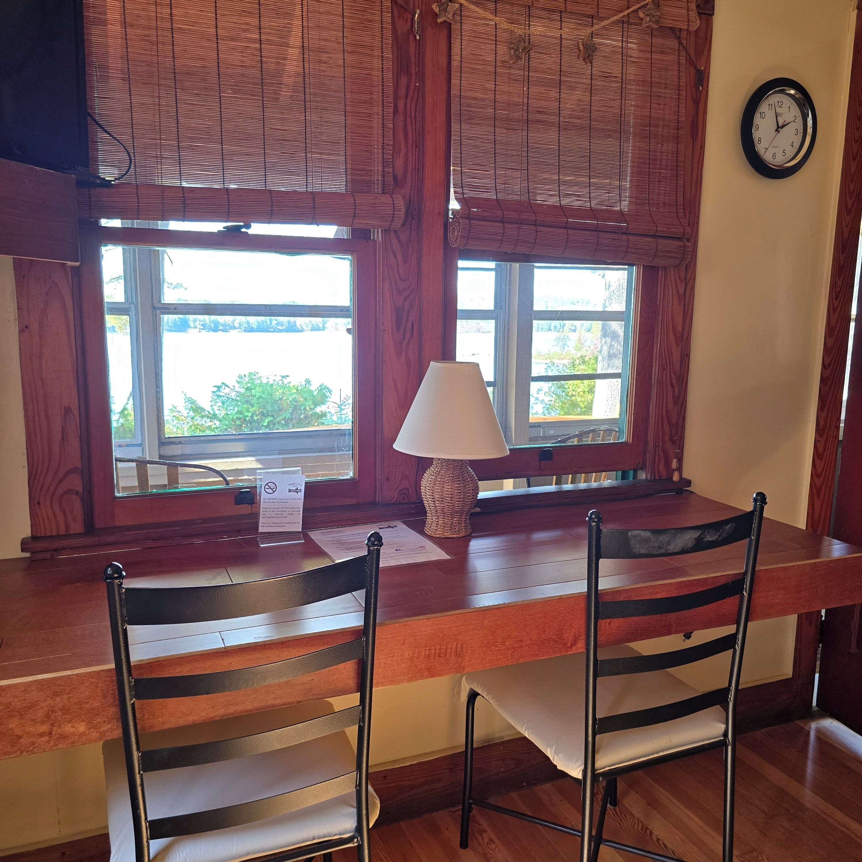 Una mesa de comedor de madera con dos sillas, una lámpara y un reloj en la pared.