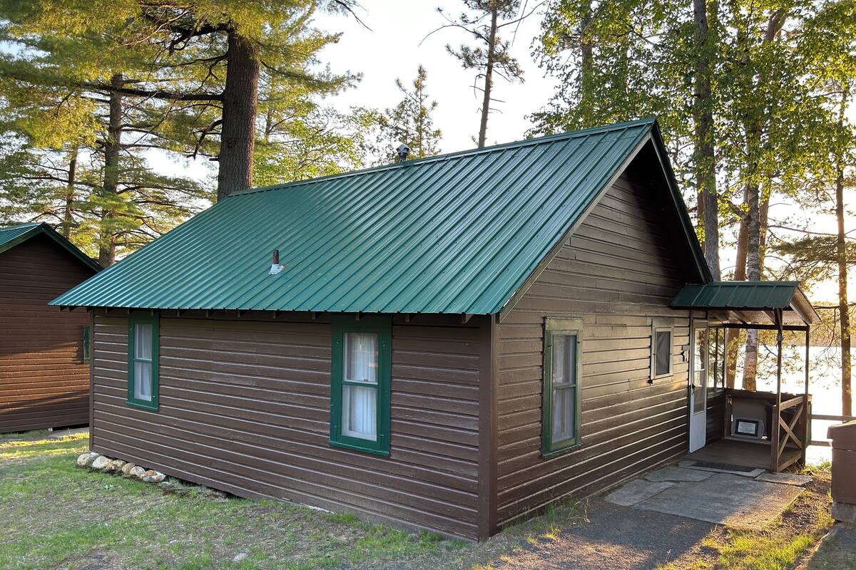 A cabin with a green metal roof, wooden siding, and a small porch area.