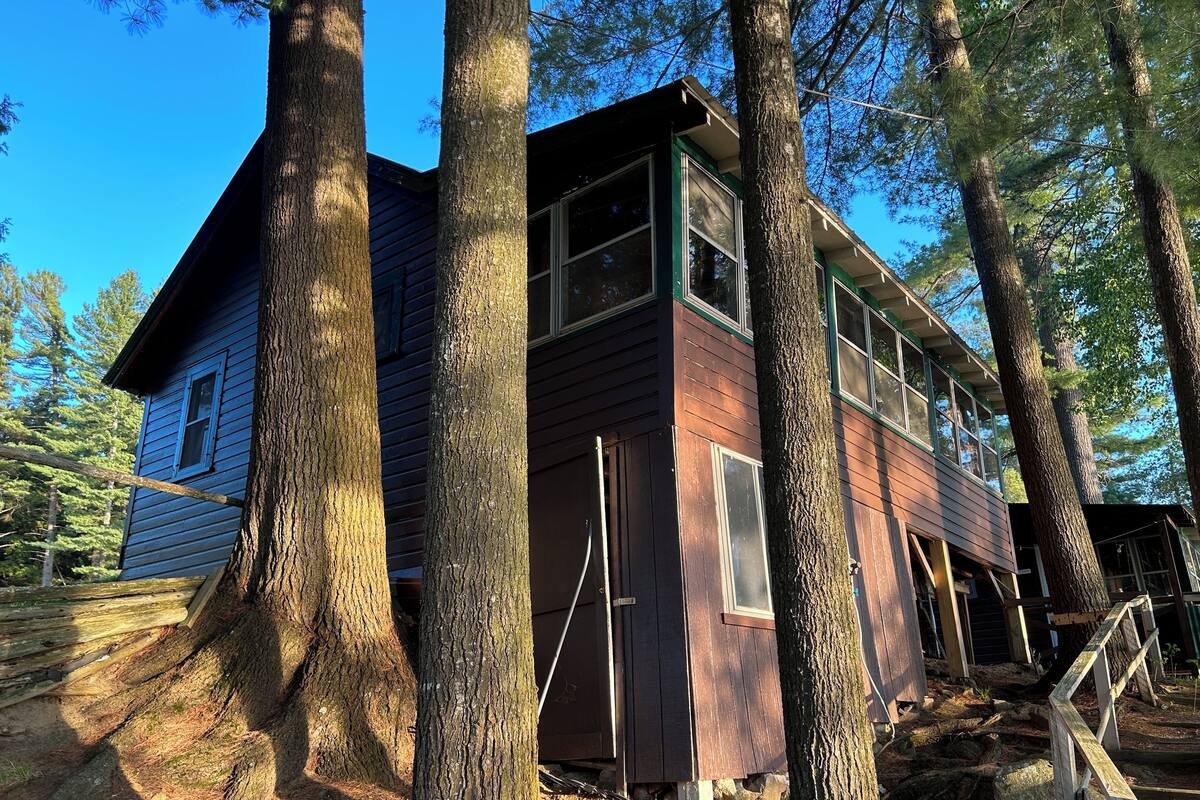 A two-story wooden cabin surrounded by large trees.