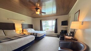 Une chambre d’hôtel avec deux lits, un bureau avec une chaise, un ventilateur de plafond et un téléviseur.