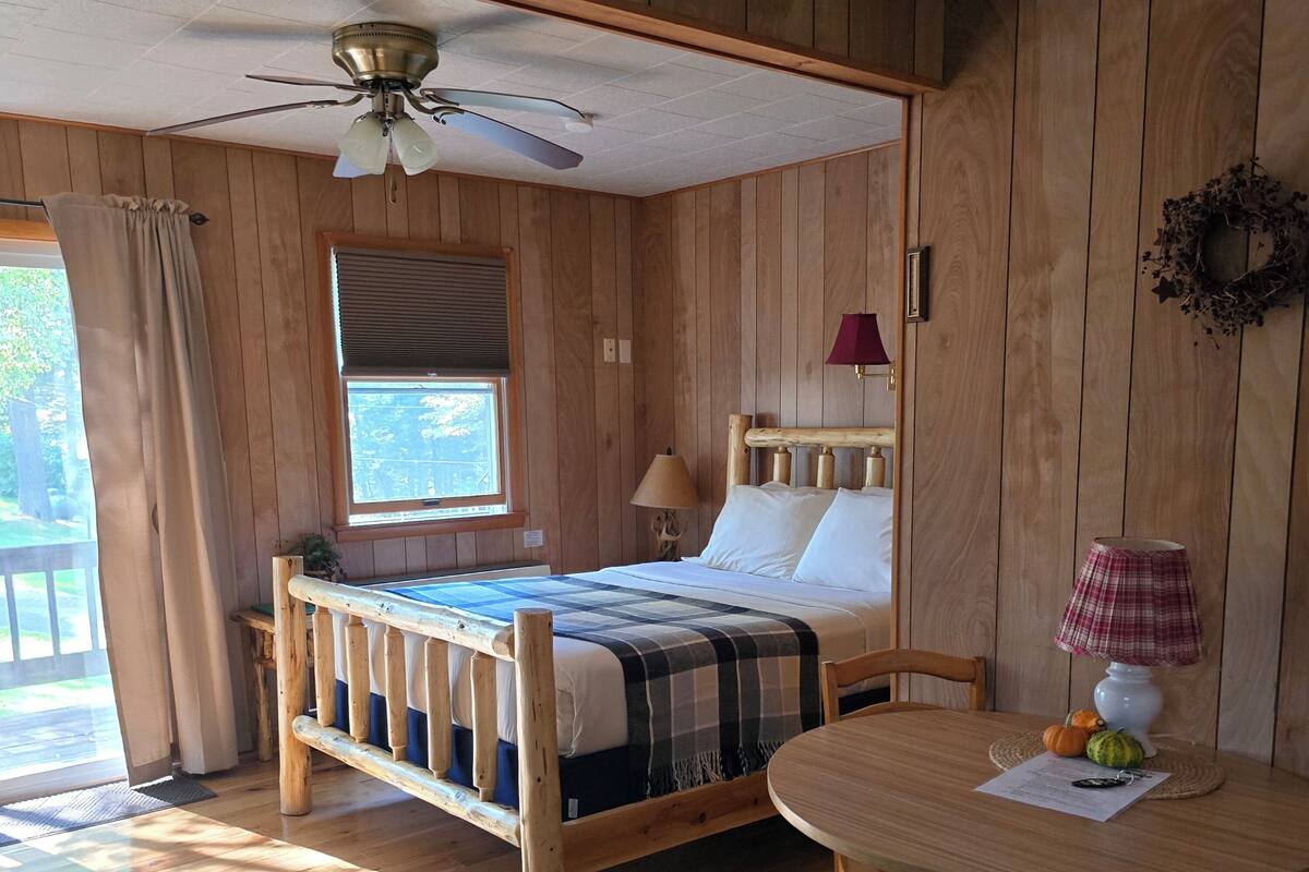 A wooden room with a bed, a table, and a ceiling fan.
