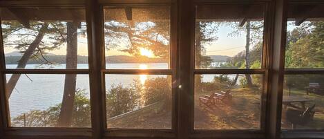 A room with three windows overlooking a lake and a dock with chairs.