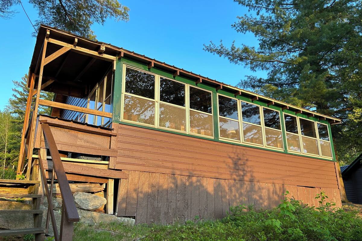A rustic wooden cabin with a balcony, surrounded by greenery.
