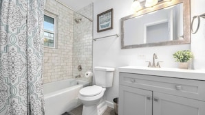 A bathroom with a bathtub, toilet, and vanity with a mirror.