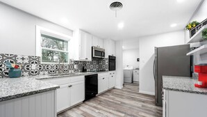 A modern kitchen with white cabinetry, a granite countertop, a built-in microwave, and a stainless steel refrigerator.