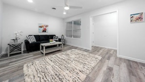 A modern living room with a black sofa, a wooden coffee table, a fluffy rug, and a ceiling fan.