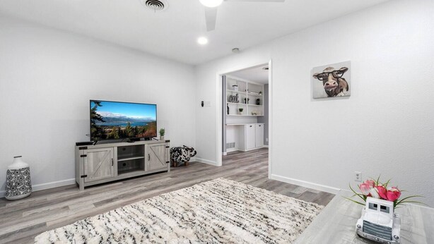 A modern living room with a flat-screen TV, a ceiling fan, a white rug, and a small table with a vase.