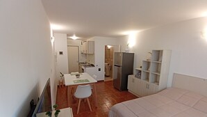 Et lille hotelværelse med seng, et spisebord med stole, tekøkken og badeværelse, der kan ses igennem en åben dør.