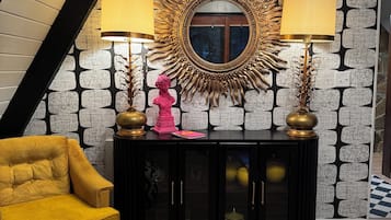 Un salon moderne avec une console noire, deux lampes, une sculpture en buste rose et un fauteuil jaune.
