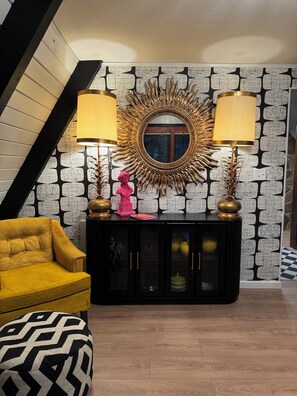 Una sala de estar moderna con un mueble consola negro, dos lámparas, una escultura de busto rosa y un sillón amarillo.