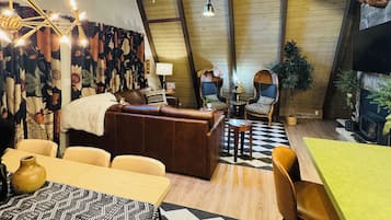 A cozy interior with a high ceiling, a fireplace, a dining area, and a seating area with a patterned rug.