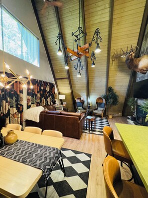 Ein gemütliches Interieur mit hoher Decke, Kamin, Essbereich und einer Sitzecke mit gemustertem Teppich.