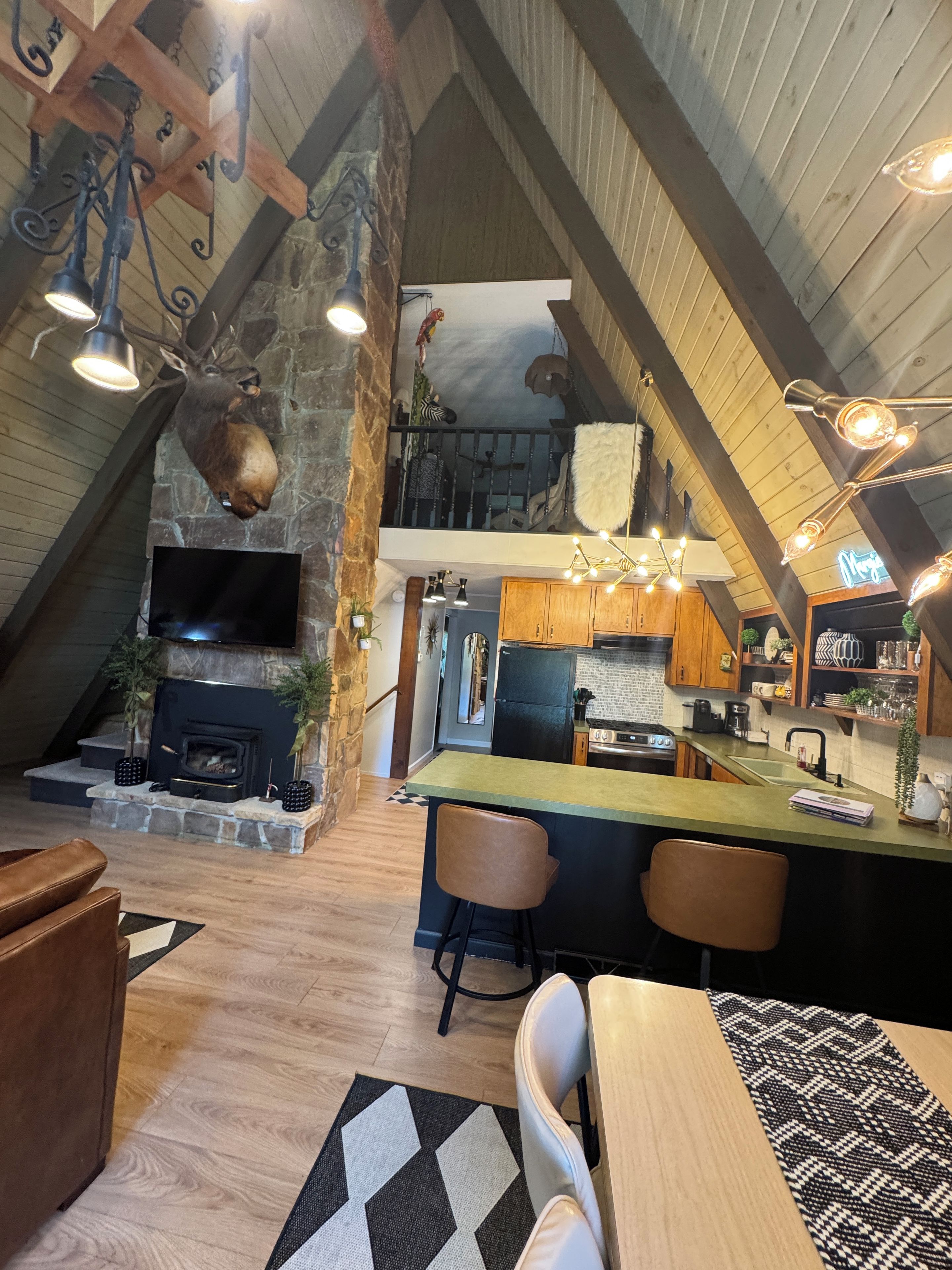A rustic interior with a stone fireplace, wooden beams, a kitchen with modern appliances, and a dining area with a bar.