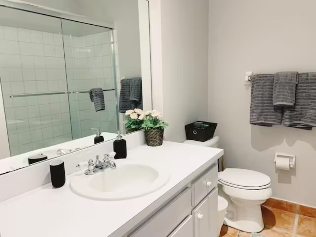 Une salle de bain moderne avec un lavabo blanc, un grand miroir, des toilettes et un porte-serviettes avec des serviettes.