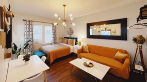 A well-lit room with a bed, a sofa, a desk, and a mirror on the wall.