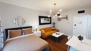 A modern hotel room with a large bed, an orange sofa, a small table, and a desk with a chair.