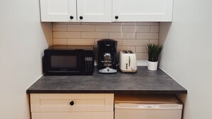 A kitchen with white cabinets, a black microwave, a coffee maker, and a toaster on a dark countertop.