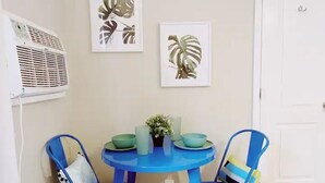 Un petit coin repas avec une table ronde et deux chaises bleues, une petite plante en pot et deux climatiseurs fixés au mur.