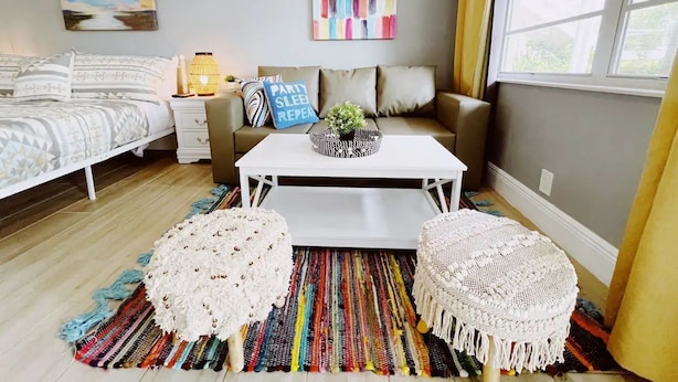 Une chambre à coucher moderne avec un lit, un canapé, une table basse et deux poufs.