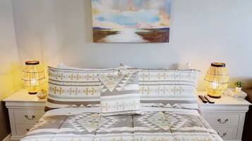 A neatly made bed with patterned bedding, two bedside lamps, and a painting above the bed.