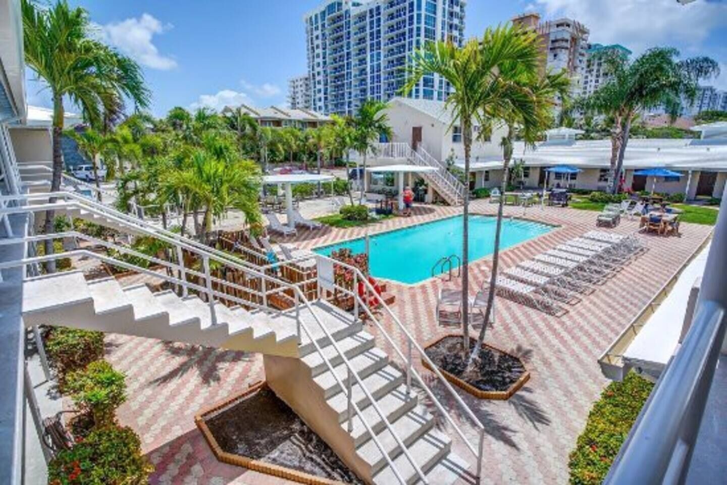 A pool area with a staircase leading to a building, surrounded by palm trees and lounge chairs.