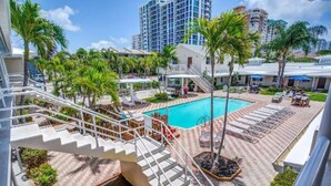 A pool area with a staircase leading to a building, surrounded by palm trees and lounge chairs. - Cozy 1 Bedroom APT 1 block off the beach W/ pool (pompano beach)