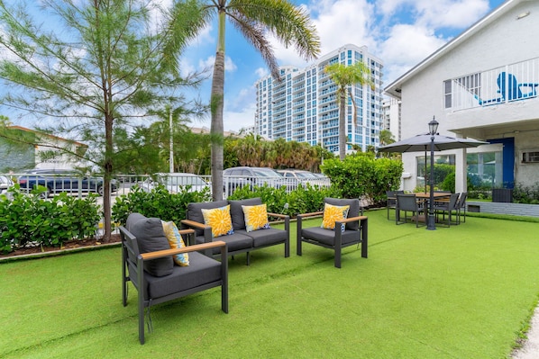 A hotel courtyard with outdoor seating, a pool, and a building with a blue logo.