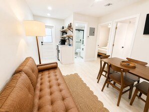 A modern living room with a brown sofa, a dining table with chairs, and a kitchen area in the background. - Cozy 2 Bedroom APT 1 block off the beach W/ pool (pompano beach)