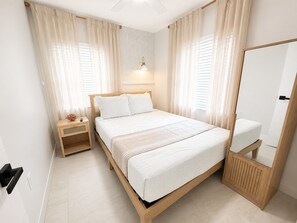 Une chambre à coucher avec un lit, des tables de chevet, un miroir et des rideaux.