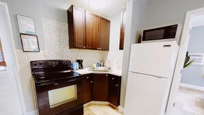 A kitchen with dark wooden cabinets, a black stove, a white refrigerator, and a tiled backsplash. - Cozy 1 Bedroom APT 1 block off the beach W/ pool (pompano beach)