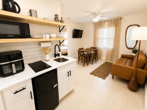 Een compacte keuken met een magnetron, koffiezetapparaat en een koelkast. Er is een eethoek met een tafel en stoelen, en een bank in de woonkamer.