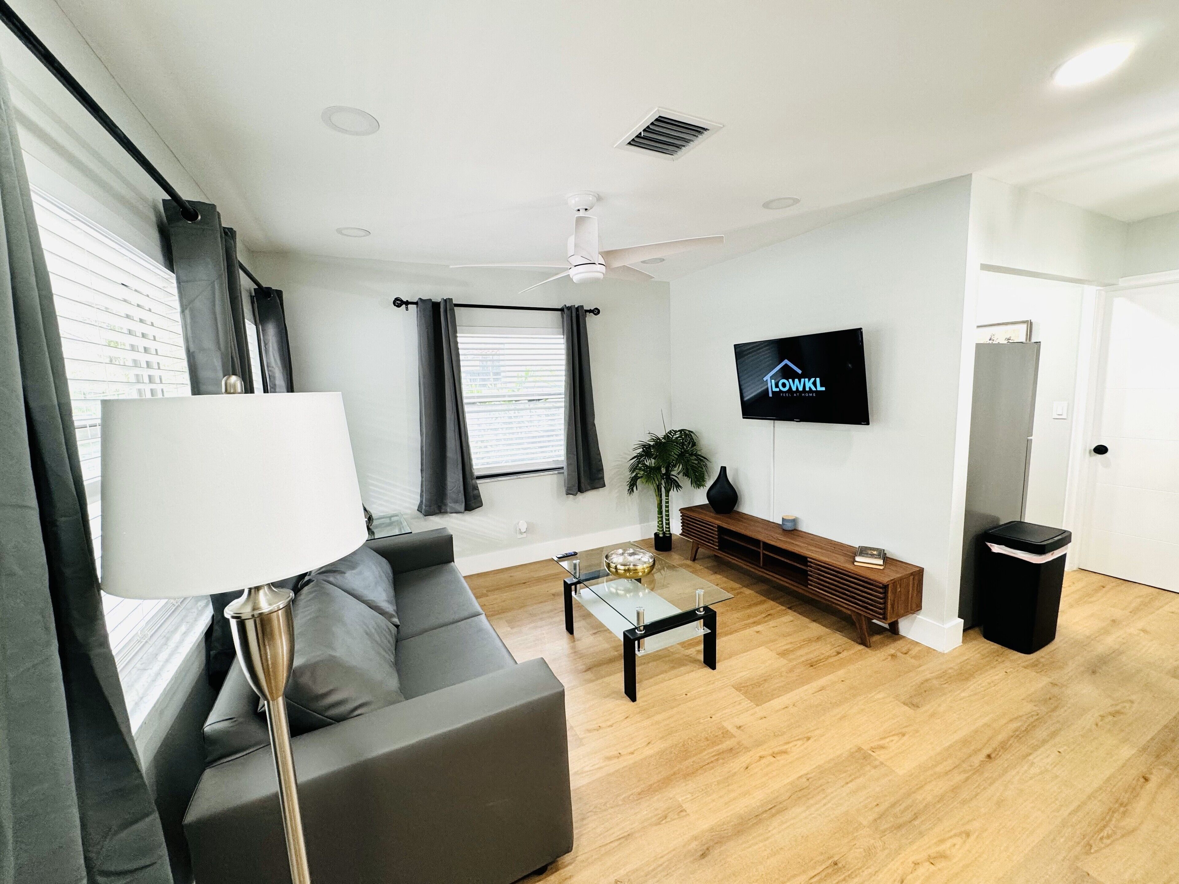 Un salon moderne avec un canapé gris, une table basse, un téléviseur et un ventilateur de plafond.