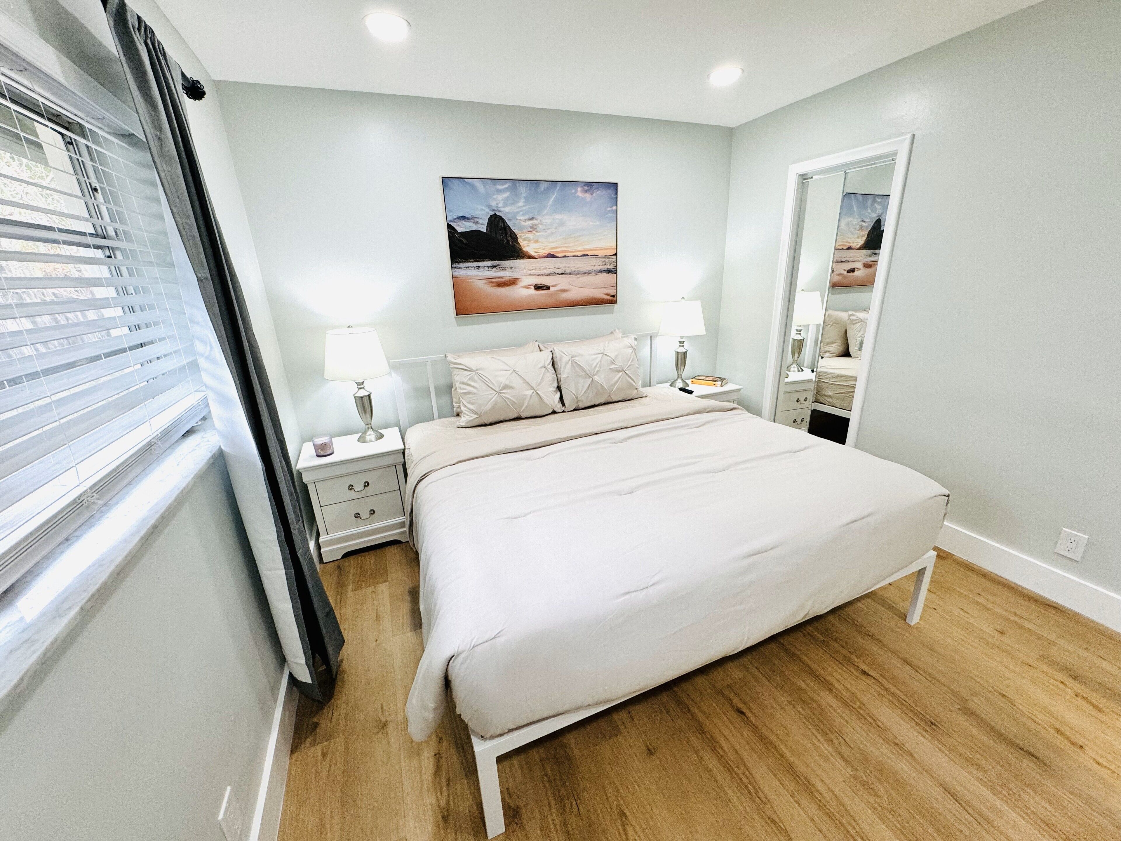 Een slaapkamer met een bed, nachtkastjes, een spiegel en een raam met zonwering.