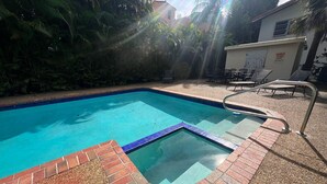 A swimming pool with a brick border and a sunshade area with chairs. - Trendy & Central 2 Bedroom Apt (Fort Lauderdale)