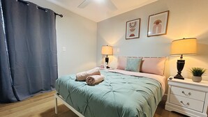 A bedroom with a bed, two bedside tables, a nightstand, a ceiling fan, and a window with a curtain. - Trendy & Central 2 Bedroom Apt (Fort Lauderdale)