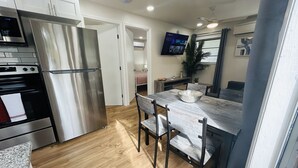 A modern kitchen with stainless steel appliances, a wooden dining table, and a flat-screen TV mounted on the wall. - Stylish & Convenient 2 BR Apt (Fort Lauderdale)