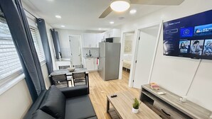 A modern living room with a black sectional sofa, a wooden coffee table, and a TV mounted on the wall displaying a Roku Channel interface. - Stylish & Convenient 2 BR Apt (Fort Lauderdale)