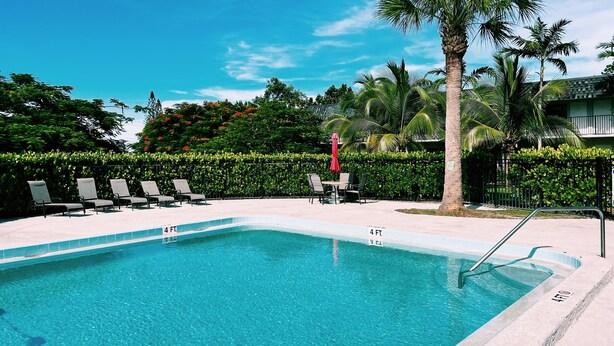 Une piscine rectangulaire dont la profondeur est indiquée par un repère à 4 pieds, entourée de chaises longues et d’un parasol rouge.