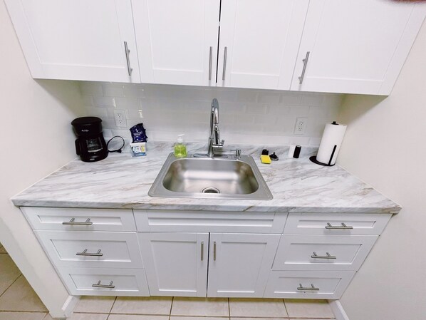 A compact kitchen with a sink, white cabinets, and a marble countertop.