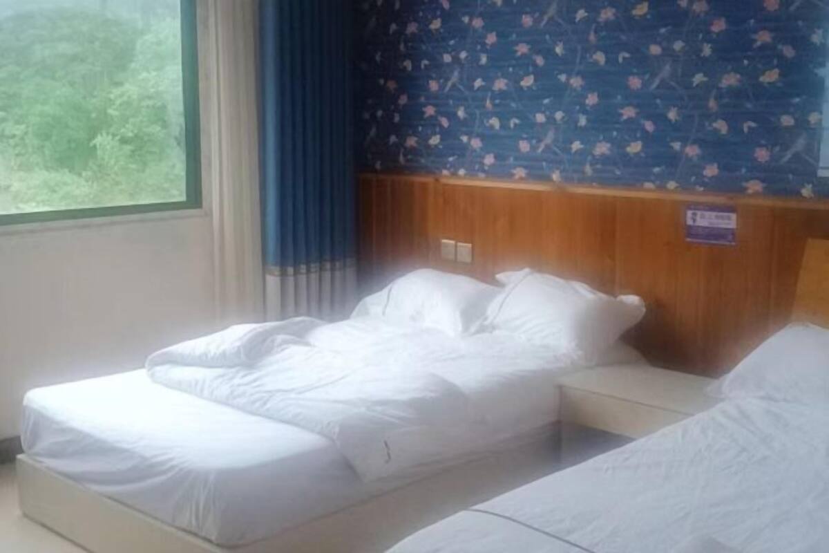 Habitación de hotel con cama, cabecera de madera, ventana con cortinas y pared con estampado floral.