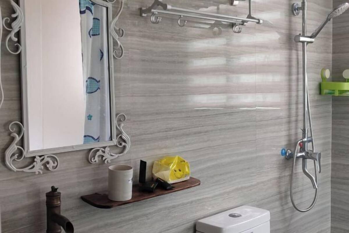 Un baño con ducha, inodoro, lavamanos, espejo y una repisa con una bolsa y una taza.