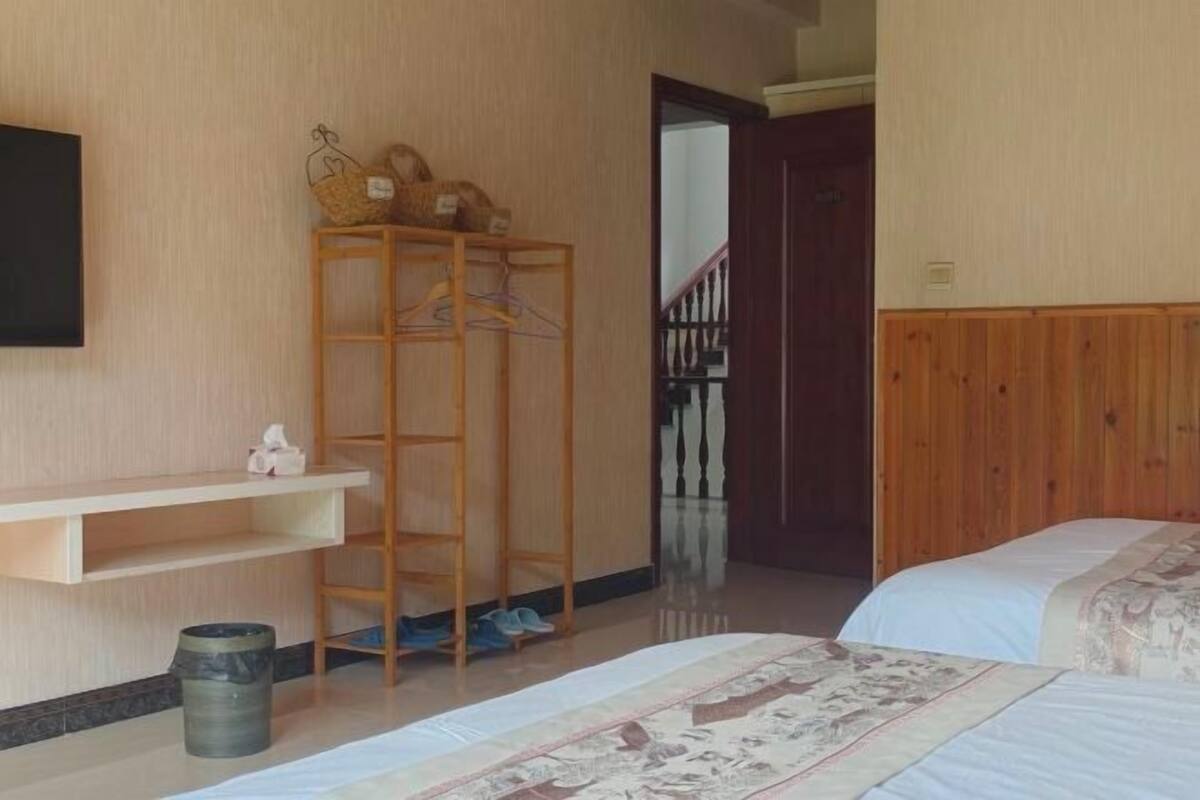 Una habitación con una cama, un estante de madera, un zapatero y una puerta que da a una escalera.