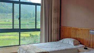A room with a large window offering a view of a green landscape, a bed with a wooden headboard, and a small table.