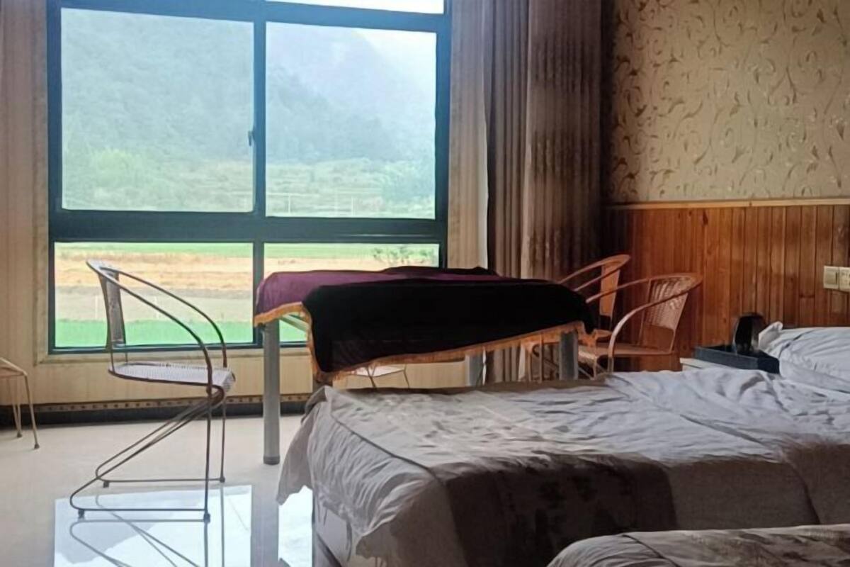 Una habitación con cama, una silla, una mesa y un ventanal con vistas al verdor.