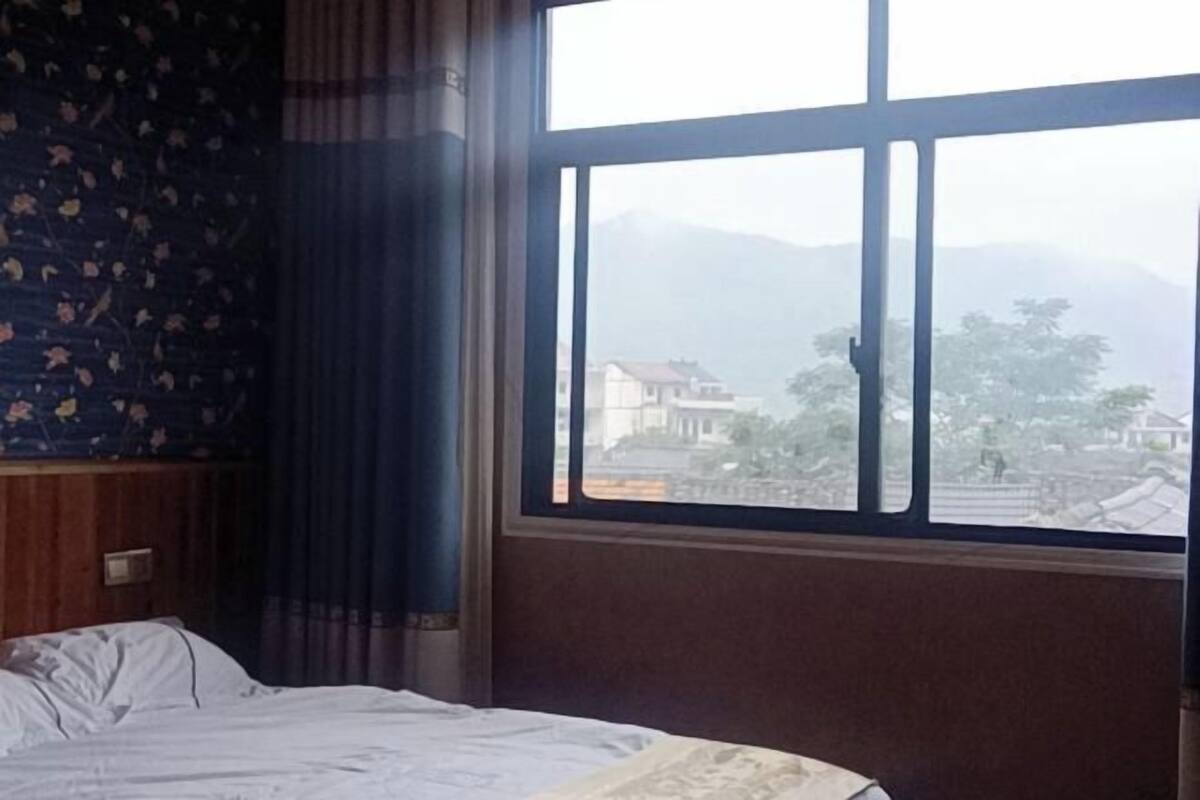 Una habitación con cama, ventana y vistas a edificios y montañas, con cortinas estampadas.
