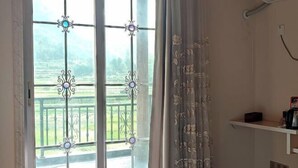 A room with a large window featuring decorative metal grilles and a view of a green landscape. There is a white shelf with a kettle and a box on it. - Xianju Stomping Songs Homestay (Xianju)