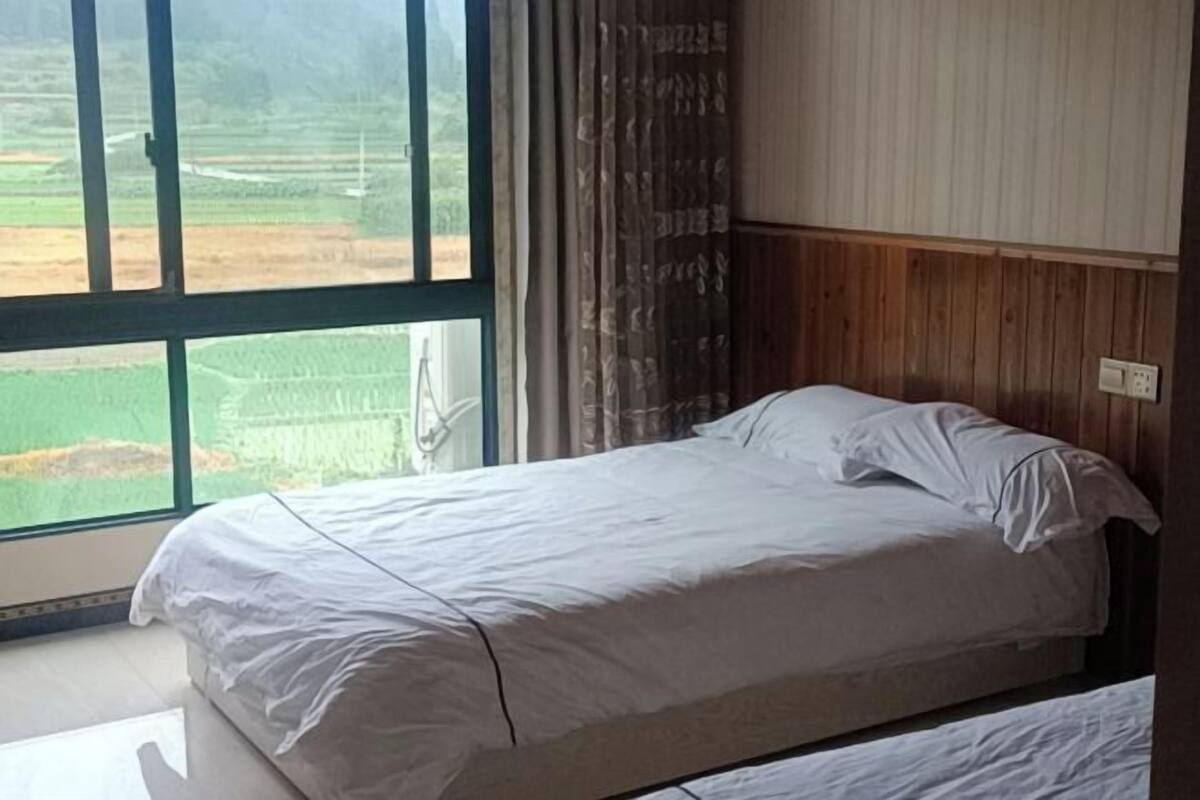 Un dormitorio con un ventanal grande, paneles de madera y una cama con ropa blanca.