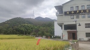 A building with a sign in a foreign language, surrounded by a rural landscape with fields and a hill in the background. - Xianju Stomping Songs Homestay (Xianju)