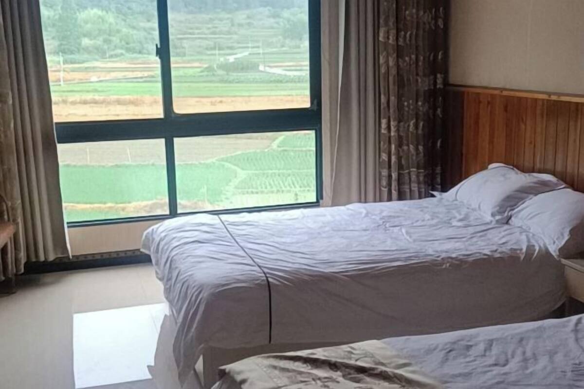 Un dormitorio con un ventanal grande, una cama, una mesita de noche y una cortina.